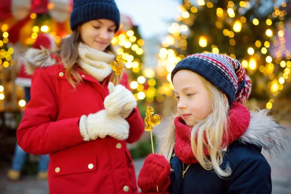 ラトビアのリガで開催される伝統的なクリスマスフェアには 鶏の形をしたロリポップを持つ2人の愛らしい姉妹 クリスマスマーケットでお菓子やキャンディー ジンジャーブレッドを楽しむ子供たち 家族や子供と冬の時間 — ストック写真