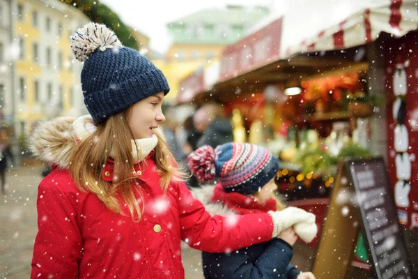 ラトビアのリガで開催される伝統的なクリスマス フェアで楽しい時間を過ごす2人の愛らしい姉妹 クリスマスマーケットでお菓子やキャンディー ジンジャーブレッドを楽しむ子供たち 家族や子供と冬の時間 — ストック写真