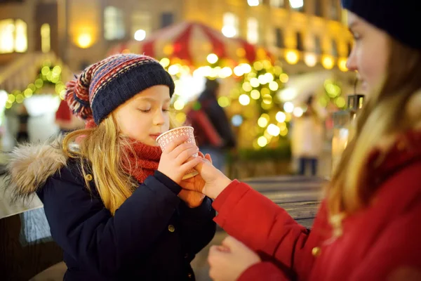 ラトビアのリガで伝統的なクリスマスフェアでホットチョコレートを飲む2人の愛らしい姉妹 クリスマスマーケットでお菓子やキャンディー ジンジャーブレッドを楽しむ子供たち 家族や子供と冬の時間 — ストック写真