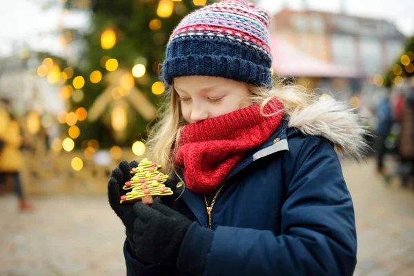 ラトビアのリガで伝統的なクリスマスフェアでジンジャーブレッドクッキーを持っているかわいい女の子 クリスマスマーケットでお菓子やキャンディー ジンジャーブレッドを楽しむ子供たち 家族や子供と冬の時間 — ストック写真