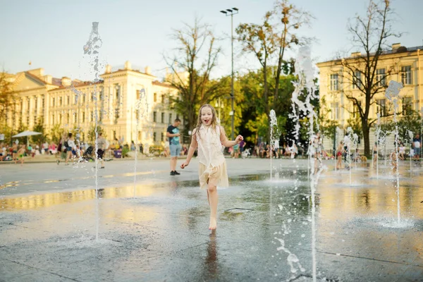 Cute young girl playing in fountains on newly renovated Lukiskes Square in Vilnius, Lithuania. Child having fun with water on sunny summer day. Active leisure for kids.