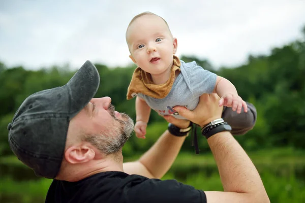 彼の父親の腕の中でかわいい赤ちゃんの男の子 市内の公園で晴れた夏の日にお父さんと息子が楽しんでいます 親愛なる息子が父親に抱かれて — ストック写真