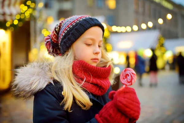 ラトビアのリガで伝統的なクリスマスフェアにストライプロリポップを持っているかわいい女の子 クリスマスマーケットでお菓子やキャンディー ジンジャーブレッドを楽しむ子供たち 家族や子供と冬の時間 — ストック写真