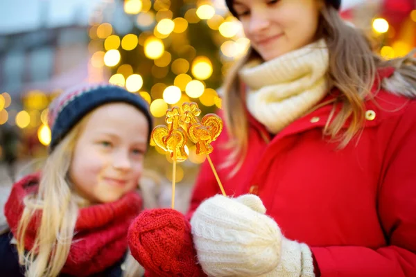 ラトビアのリガで開催される伝統的なクリスマスフェアには 鶏の形をしたロリポップを持つ2人の愛らしい姉妹 クリスマスマーケットでお菓子やキャンディー ジンジャーブレッドを楽しむ子供たち 家族や子供と冬の時間 — ストック写真