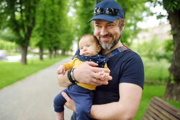 彼の父親の腕の中でかわいい赤ちゃんの男の子 市内の公園で晴れた夏の日にお父さんと息子が楽しんでいます 親愛なる息子が父親に抱かれて — ストック写真