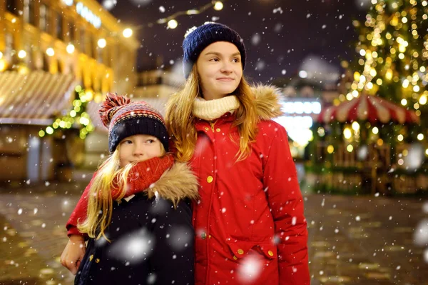 ラトビアのリガで開催される伝統的なクリスマス フェアで楽しい時間を過ごす2人の愛らしい姉妹 クリスマスマーケットでお菓子やキャンディー ジンジャーブレッドを楽しむ子供たち 家族や子供と冬の時間 — ストック写真