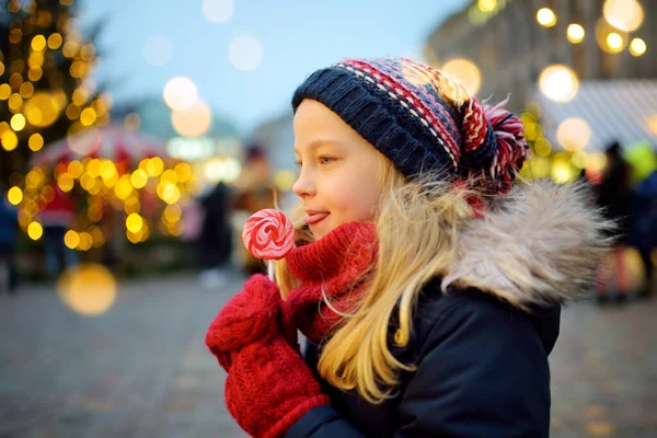 ラトビアのリガで伝統的なクリスマスフェアにストライプロリポップを持っているかわいい女の子 クリスマスマーケットでお菓子やキャンディー ジンジャーブレッドを楽しむ子供たち 家族や子供と冬の時間 — ストック写真