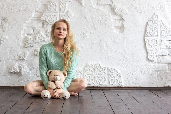 Beautiful young woman with toy bear sits on the floor of the room.