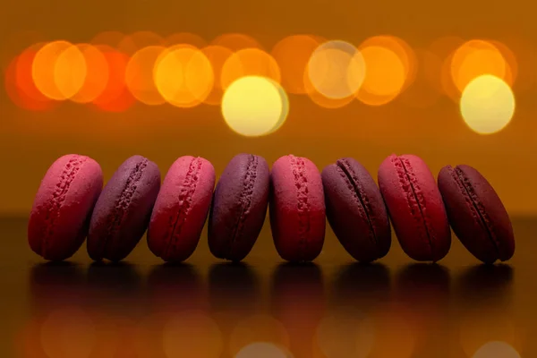 A row of pink and chocolate macaroon pies on the background of holiday lights closeup.