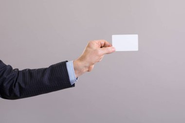 El gri bir arka plan üzerinde boş bir kart ile işadamı.