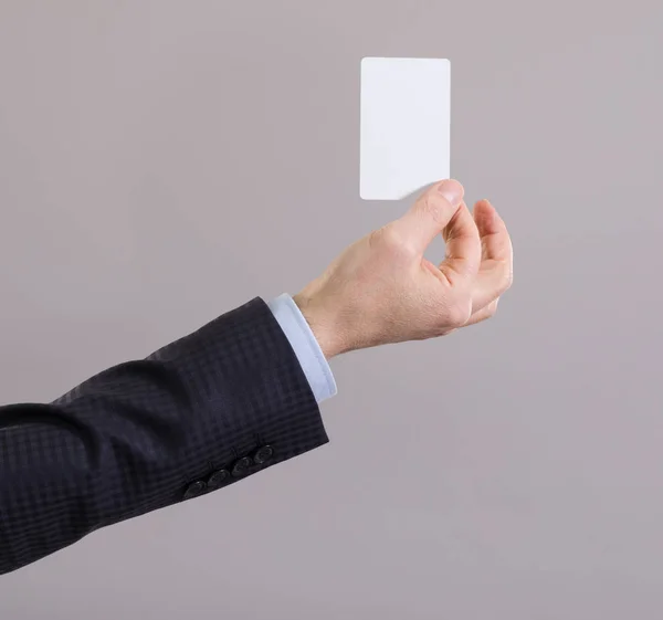 Mão de um homem de negócios com um cartão em branco em um fundo cinza . — Fotografia de Stock