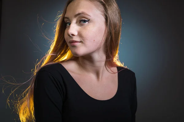 Portrait of a young woman with light sunlit hair on a dark background.