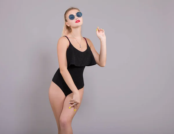 性感的年轻女子在黑色泳衣和太阳镜上摆出浅灰色背景 女性沙滩时尚 — 图库照片
