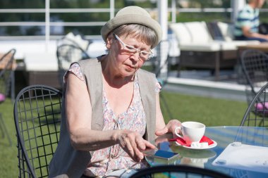 Yaşlı bir kadın bir yaz açık kafede otururken bir akıllı telefon kullanır.