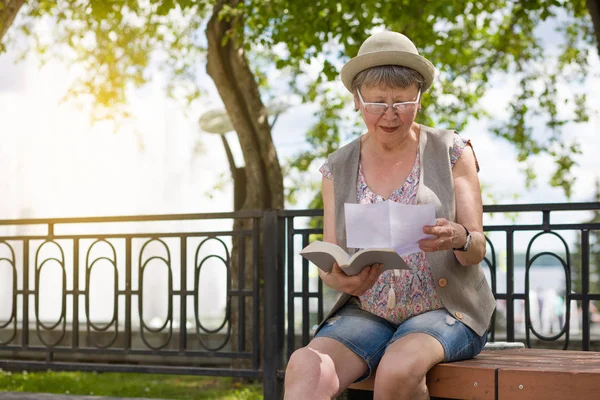 夏に公園のベンチに座って手紙や書類を読む高齢の女性 — ストック写真