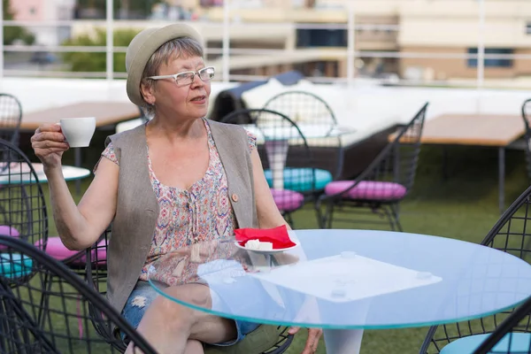 一位老年妇女坐在夏季户外咖啡馆里享用一杯咖啡 — 图库照片