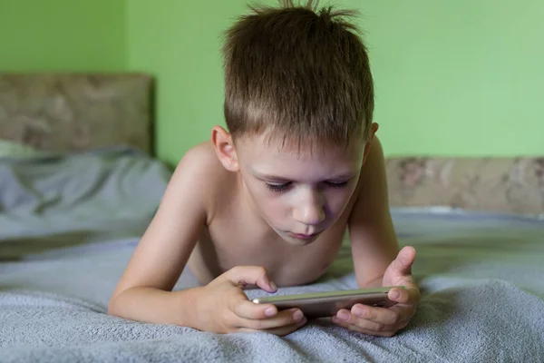 Malý Chlapec Soustředěně Dívá Obrazovku Svého Mobilního Telefonu Ležícího Doma — Stock fotografie