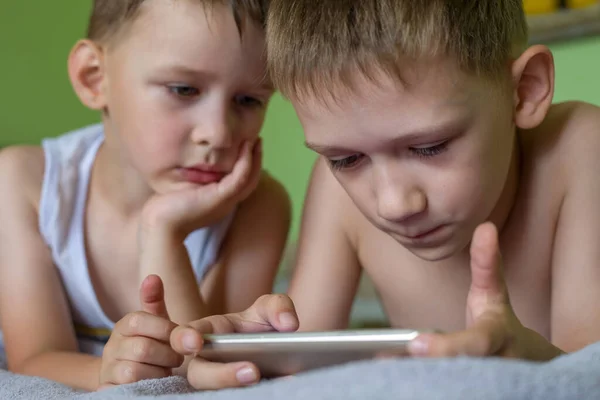 Dva Malí Chlapci Soustředěně Dívají Obrazovku Svého Mobilního Telefonu Ležícího — Stock fotografie