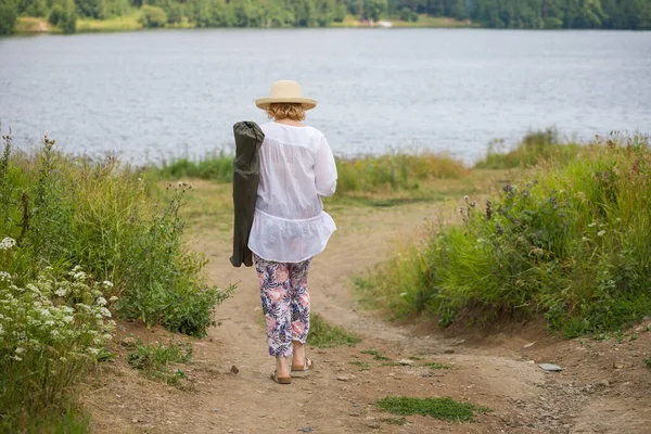 一位老年妇女沿着乡间小路散步 享受着夏日的自然 老年人积极生活方式的概念 — 图库照片