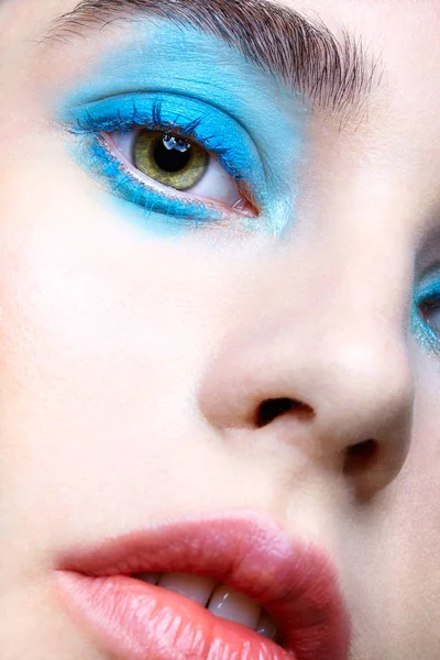 Closeup macro portrait of female face. Human woman half-face with unusual beauty makeup. Girl with perfect skin, green pistachio colour eyes and blue shadows  make-up.