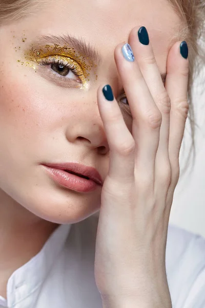 Closeup shot of  human female face. Woman with unusual glitter glitzy vogue face beauty makeup. Girl with yellow smoky eyes eye shadows and hand near face