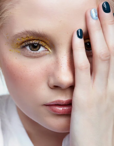 Closeup shot of  human female face. Woman with unusual glitter glitzy vogue face beauty makeup. Girl with yellow smoky eyes eye shadows and hand near face
