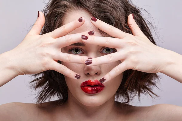 Beauty portrait of young woman with hands on face. Brunette girl with unusual alyapy red female face makeup.