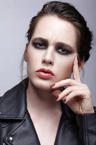 Portrait of female in black leather jacket. Woman with unusual beauty evening makeup. Girl with perfect skin, green pistachio colour eyes and violet - black shadows make-up.