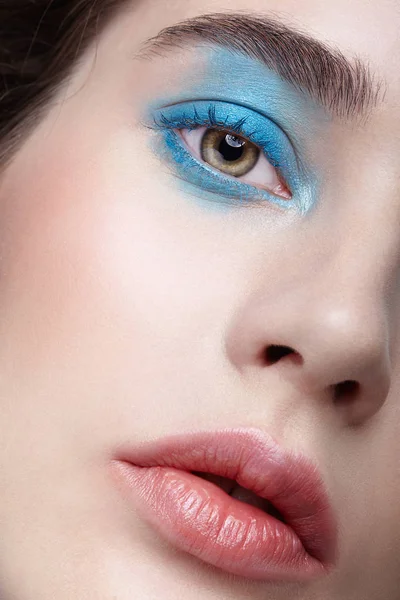 Closeup macro portrait of female face. Human woman half-face with unusual beauty makeup. Girl with perfect skin, green pistachio colour eyes and blue shadows make-up.