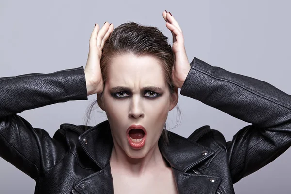 Portrait of female in black leather jacket and mouth open. Woman with unusual beauty evening makeup. Girl with perfect skin, green pistachio colour eyes and violet - black shadows make-up.
