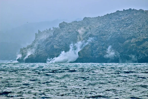 Okhotsk Sea, Chirpoy Island, Snow volcano activity, Russia. Hot volcanic lava falls into the sea. White fog rises over the shore.