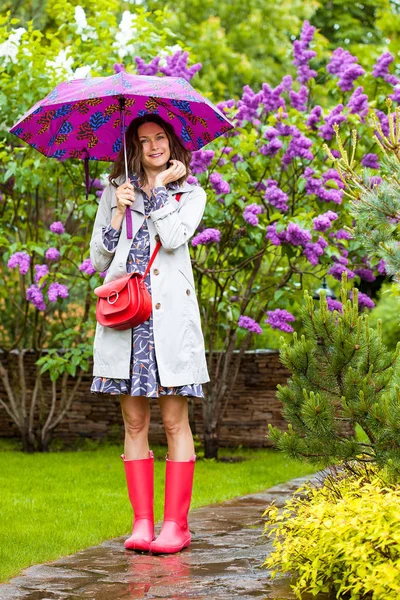 Beautiful middle aged woman in a light raincoat and with an umbr