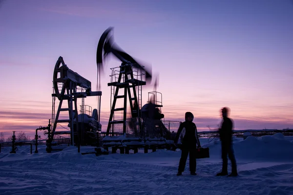 Oil workers in oilfield. Pump jack and engineer on a winter sunset sky background. Western Siberia.