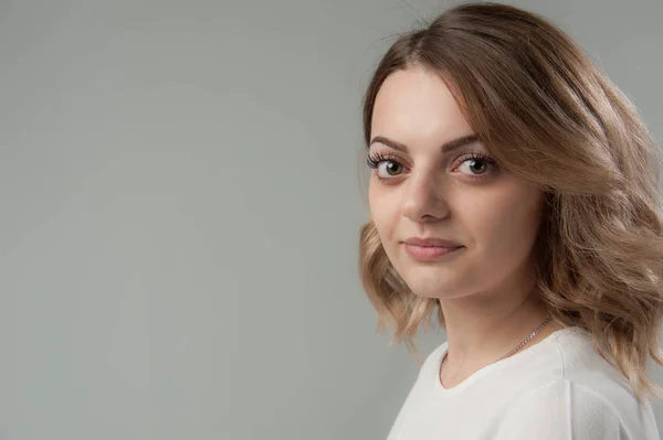 Retrato de uma jovem mulher atraente com cabelo loiro em um fundo cinza neutro . — Fotografia de Stock