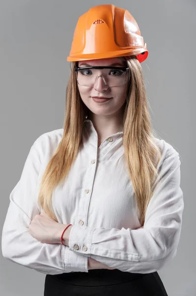 Retrato de uma jovem mulher atraente com cabelo loiro em capacete laranja em um fundo cinza neutro . — Fotografia de Stock