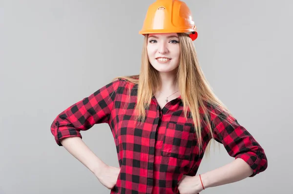 Retrato de uma jovem mulher atraente com cabelo loiro em capacete laranja em um fundo cinza neutro . — Fotografia de Stock