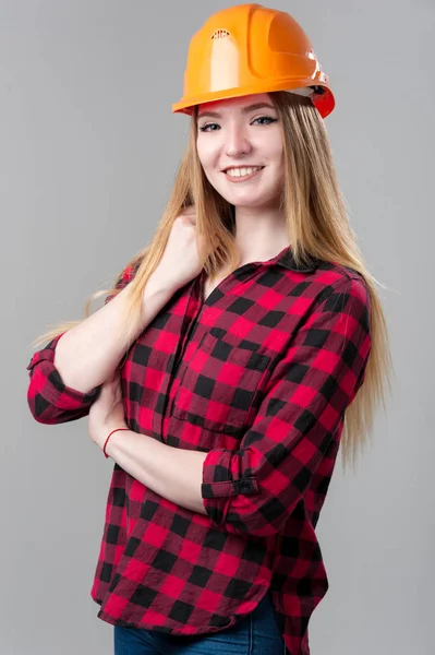 Retrato de uma jovem mulher atraente com cabelo loiro em capacete laranja em um fundo cinza neutro . — Fotografia de Stock