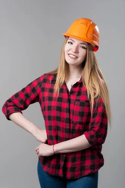 Πορτρέτο μιας νεαρής ελκυστική γυναίκα με ξανθά μαλλιά σε πορτοκαλί κράνος σε ουδέτερο γκρι φόντο. — Φωτογραφία Αρχείου