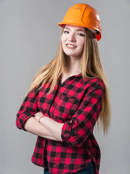 중립 회색 배경에 오렌지 헬멧에 금발 머리를 가진 젊은 매력적인 여자의 초상화. — 스톡 사진