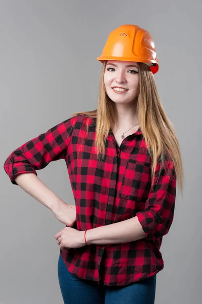 Retrato de uma jovem mulher atraente com cabelo loiro em capacete laranja em um fundo cinza neutro . — Fotografia de Stock