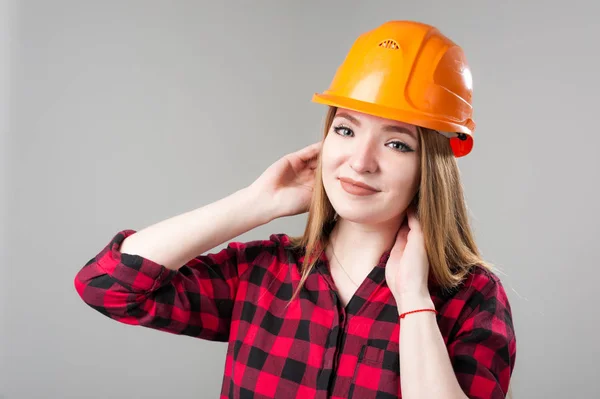 Retrato de uma jovem mulher atraente com cabelo loiro em capacete laranja em um fundo cinza neutro . — Fotografia de Stock