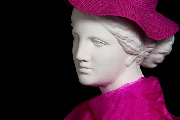 Plaster copy of ancient statue head in pink hat and scarf on a black background. Gypsum sculpture female face. — Stock Photo, Image
