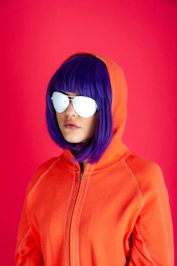 Parlak pembe arka planda mavi saçlı alternatif funky kız. Kapüşonlu ve beyaz gözlüklü güzel bir kadının moda portresini kapat. Sıra dışı gençlik modası konsepti. Sıcak resim.