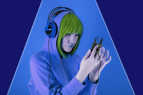 Portrét krásná mladá funky žena se zelenými žlutými vlasy na modrém pozadí. Dívka se sluchátkem poslouchá příjemnou hudbu ve svém smartphonu. Koncepce umění koláž v současném stylu pop art. — Stock fotografie