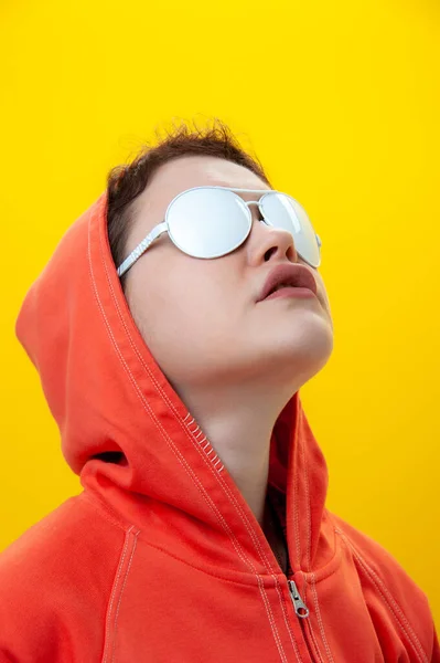 Primer plano retrato de moda joven hermosa mujer en sudadera con capucha y gafas blancas. Chica funky alternativa sobre un fondo amarillo brillante. Concepto inusual de moda juvenil. Imagen caliente. — Foto de Stock