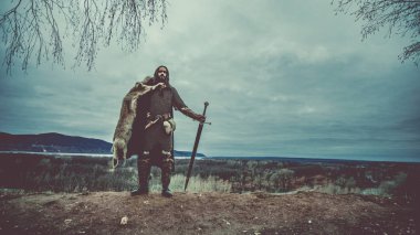 Uzun saçlı knight iki elle kılıç ile. Ortaçağ kırsal arka plan.