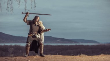 Uzun saçlı knight iki elle kılıç ile. Ortaçağ kırsal arka plan.