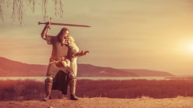 Uzun saçlı knight iki elle kılıç ile. Ortaçağ kırsal arka plan.
