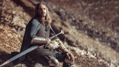 Uzun saçlı knight iki elle kılıç ile. Kayaların üzerinde arka plan.