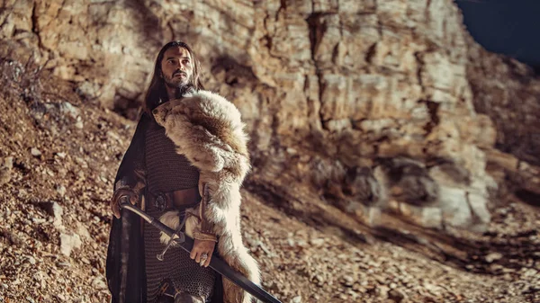 长头发的骑士用双手剑 背景上的岩石 — 图库照片